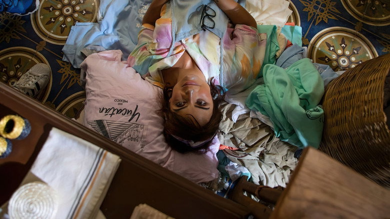 A woman in a bright, chaotic apartment, surrounded by fabric swatches and half-finished designs, her expression caught between frustration and exhaustion