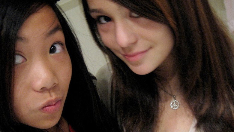 A dimly lit bedroom, the glow of a laptop screen casting shadows on a teenage girl's face as she stares at the screen, her expression unreadable.