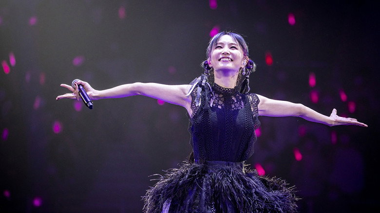 A dimly lit stage, LiSA mid-performance, her silhouette framed by warm backlighting, the crowd a blur of hands raised in unison.