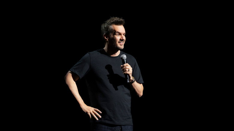 Jim Jefferies on stage, mid-performance, gesturing with his hands as he delivers a punchline.