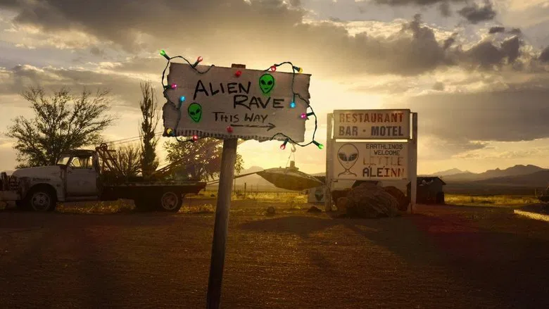 A wide shot of the Nevada desert at dusk, the vast emptiness stretching toward the horizon, with a handful of tents and cars clustered near the edge of Area 51’s perimeter.