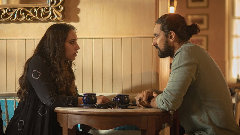 A dimly lit room where two strangers sit across from each other, the glow of a phone screen casting long shadows on their faces
