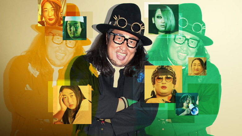 Akiyama stands in front of a green screen, his expression unreadable, as if waiting for the joke to reveal itself.