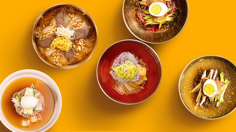 A close-up of hands pulling translucent noodles from a steaming pot, the dough stretching like taffy