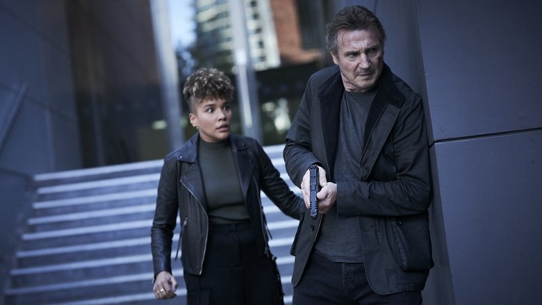 A wide shot of Liam Neeson walking through an empty, modern city square, emphasizing his isolation within the frame.