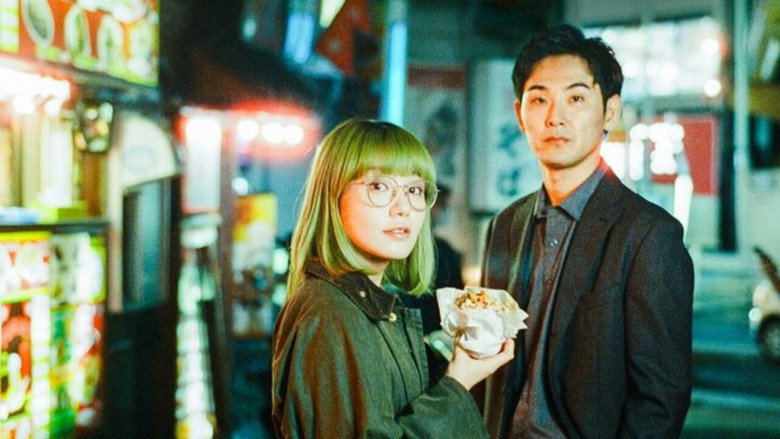 Mari and Ryo sit across from each other at a tiny restaurant table, steam rising from a shared bowl of ramen between them. The warm light catches Mari's green hair as she grins, while Ryo's expression remains unreadable, his chopsticks hovering over the broth.