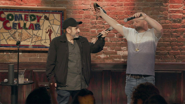 Two comedians on stage, one mid-laugh, the other with a skeptical smirk