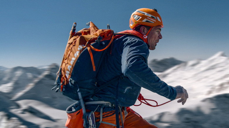 A climber's gloved hand grips a jagged rock face, the vast expanse of the Alps stretching out below in a dizzying drop.
