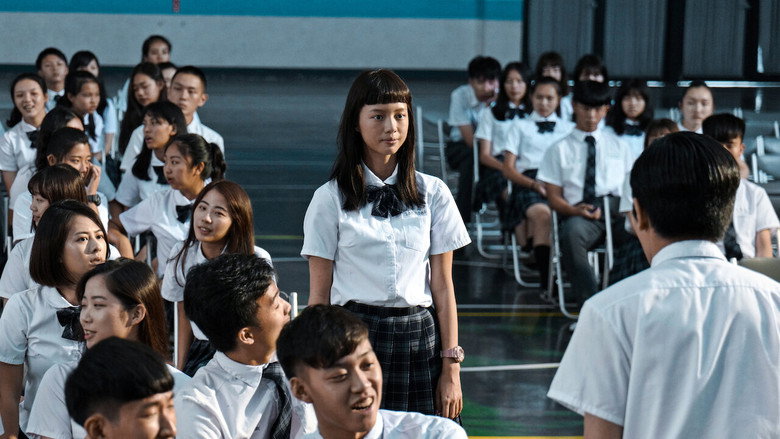 A group of students huddled in a dimly lit hallway, their faces half-hidden in shadow, whispering as one girl stands apart, her posture rigid with humiliation.