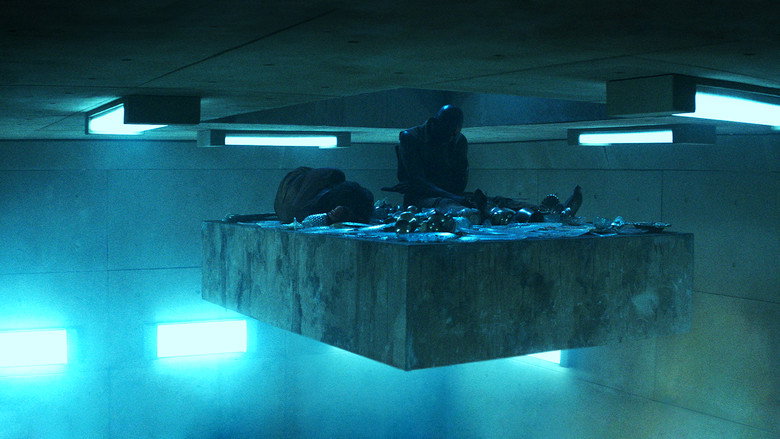 A prisoner stares upward at the descending platform, his face half-lit by the dim glow of the food above