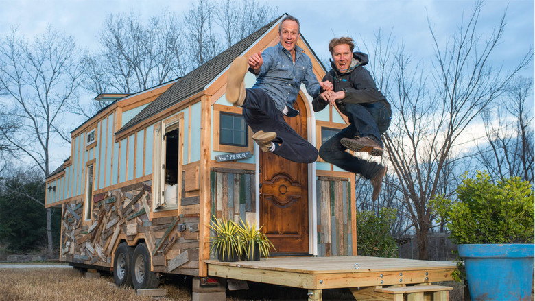 A family stands in front of their newly built tiny home, arms crossed, grinning like they’ve just won the lottery