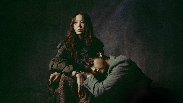 A dimly lit interrogation room where Jung Yi-shin, seated and unshackled, leans forward with eerie calm, her face half in shadow as she speaks to her son, Detective Cha Su-yeol.