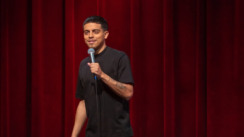 Ralph Barbosa on stage in a black shirt, bathed in pink light, mid-gesture during his stand-up set