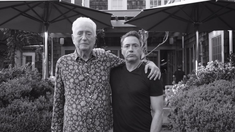 A black-and-white still of Robert Downey Sr. mid-conversation, his hands animated, his expression caught between laughter and something more contemplative.