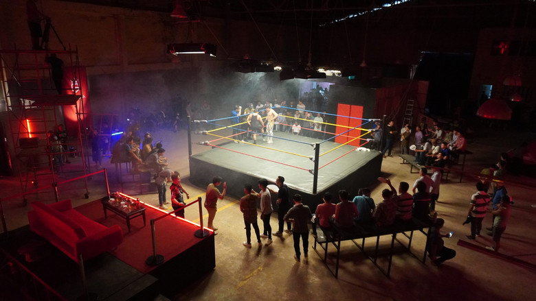 A wrestler in a fuchsia mask and sequined singlet mid-air, arms outstretched, as the crowd blurs into a neon haze