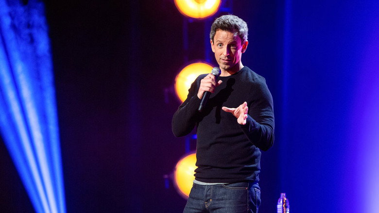 Seth Meyers on stage, mid-gesture, his face lit with the kind of exaggerated surprise that suggests he’s about to deliver a punchline.