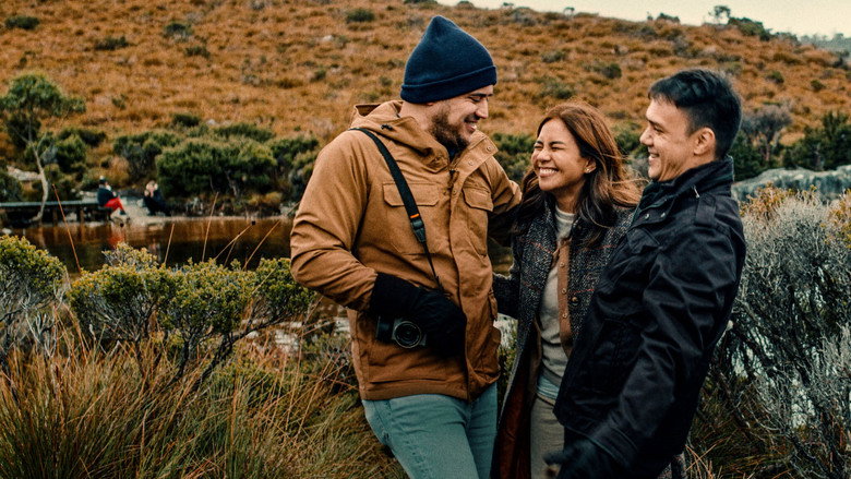 Three friends stand on a windswept cliff in Tasmania, the ocean stretching endlessly behind them