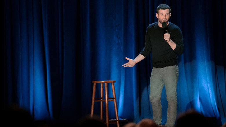 Brent Morin mid-joke, hands gesturing, under the warm glow of stage lights