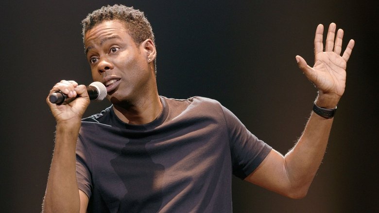 Chris Rock mid-performance, his face half-lit by stage lights, a smirk playing at the edges of his mouth.