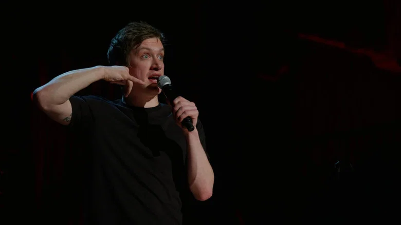 A dimly lit stage, Sloss mid-gesture, his face half in shadow, the audience a blur of faces caught between laughter and unease.