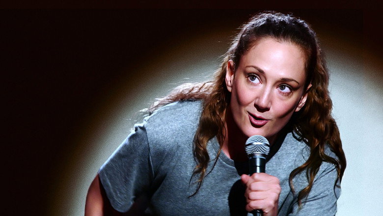 Novak mid-monologue, microphone cord coiled around her wrist like a lifeline, stage lights casting long shadows behind her