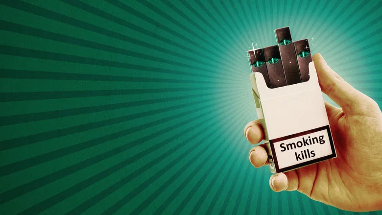 A close-up of a Juul device, its sleek metallic surface reflecting light, resting on a table next to a pack of cigarettes.