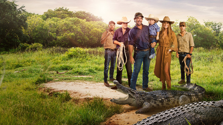 A crocodile's massive jaws are pried open by gloved hands, its yellowed teeth glinting in the harsh Australian sun.