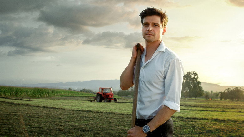 A wide shot of the farm at dusk, the golden light stretching across the fields, the house small against the horizon