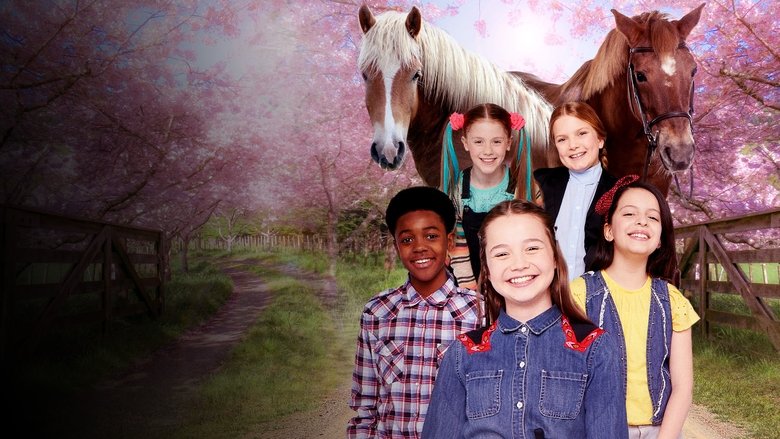 A group of kids in riding helmets stand in a sunlit stable, brushing a pony while one girl holds a lead rope with careful hands.