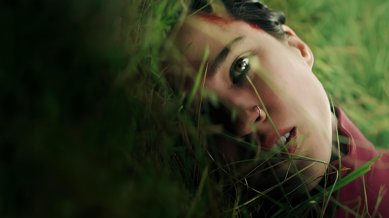 A shadowy figure looms over a woman lying on the forest floor, her face half-lit by flickering light.