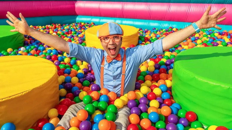 Blippi and Meekah stand in front of a massive inflatable bounce house, their arms outstretched as an excavator dumps thousands of colorful ball pit balls into the structure.