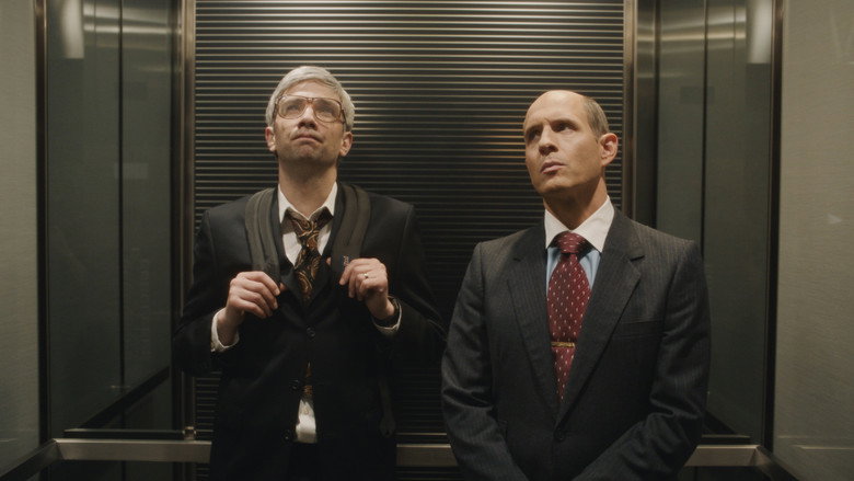 A dimly lit boardroom, where three men in suits huddle around a prototype, their faces lit by the glow of a tiny screen.