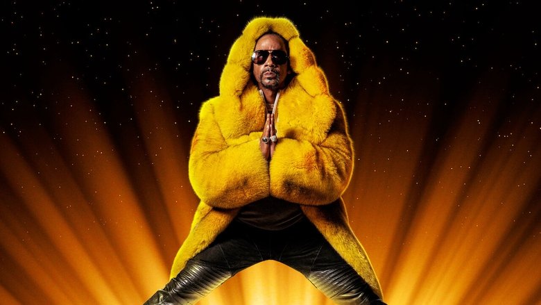 Katt Williams on stage in a white suit, mid-performance, arms outstretched