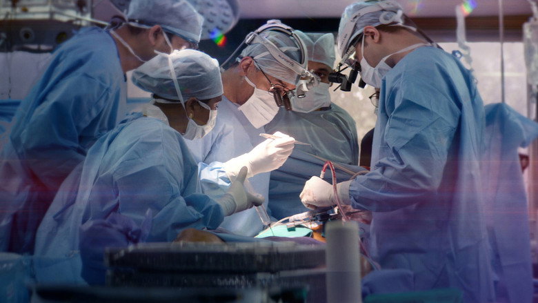 A surgeon in scrubs stands in an operating room, his face half-lit by the sterile glow of surgical lights