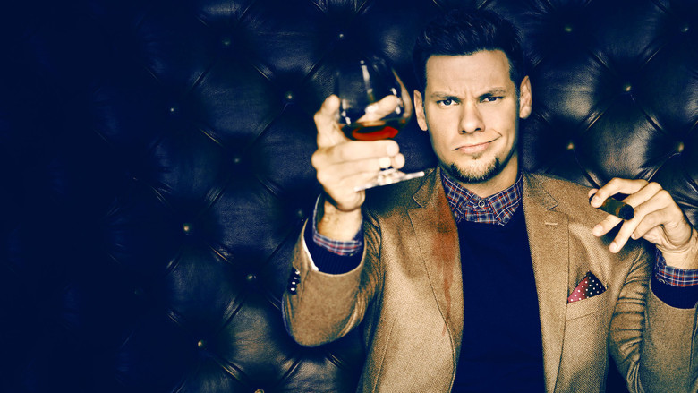 Theo Von on stage, bathed in warm light, mid-gesture with a bemused expression