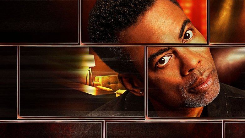 Chris Rock on stage, mid-gesture, bathed in warm light, the audience a blur of faces in the background
