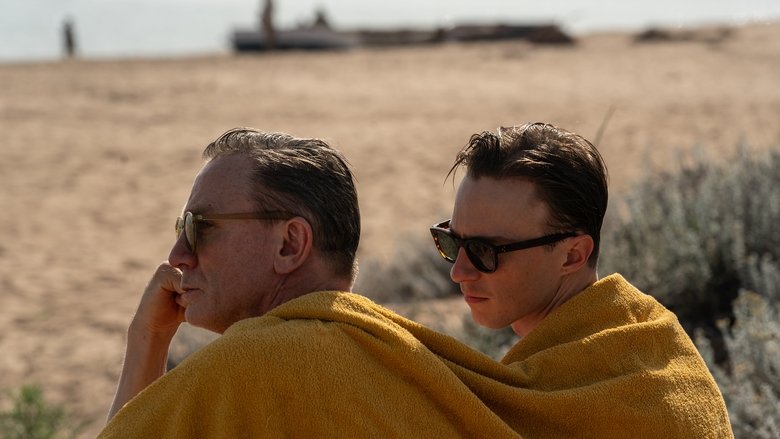 William Lee sits in a dimly lit bar, his face illuminated by a sliver of light, embodying a sense of deep, detached isolation.