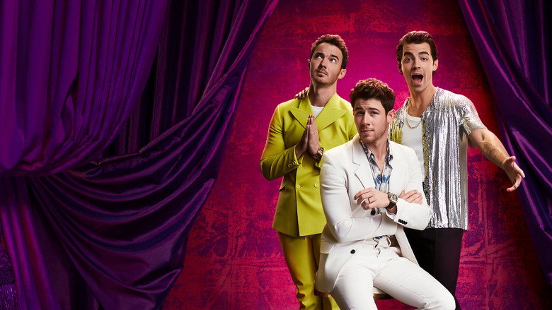 The brothers sit in a row, arms crossed, as the audience erupts in laughter behind them