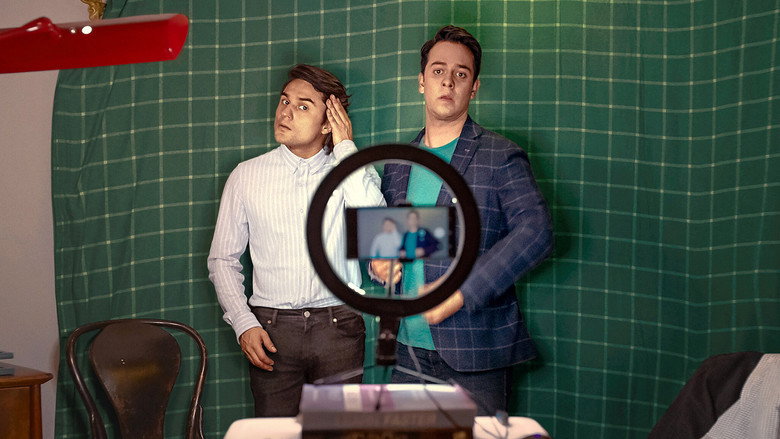 Two men in a dimly lit room, one holding a phone while the other gestures wildly, mid-drunk pitch.