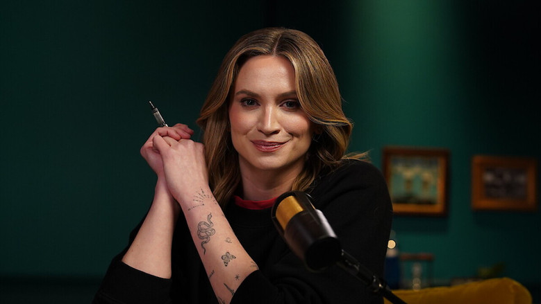 A dimly lit studio set with two empty chairs facing each other, a microphone between them, and a large screen displaying a blurred crime scene photo in the background.