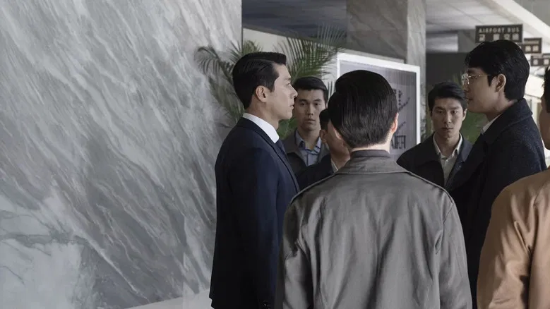 Two men in suits facing each other in a dimly lit room