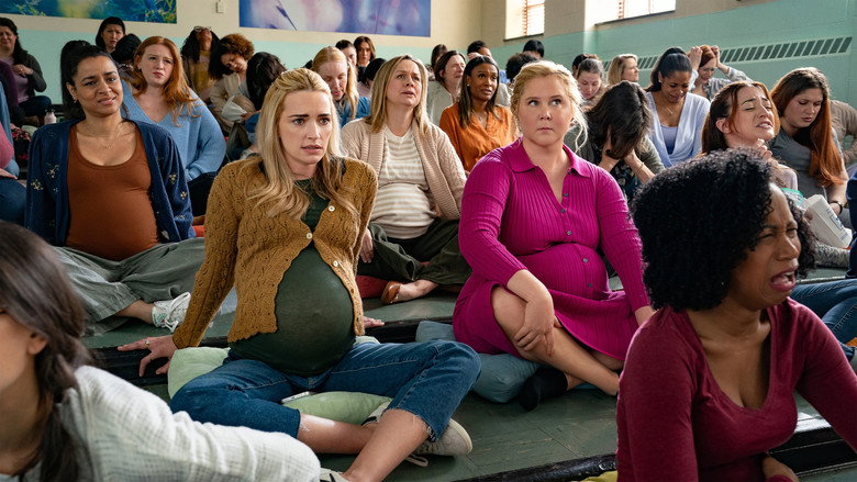 Lainy Newton (Amy Schumer) adjusting her prosthetic baby bump in a crowded subway car, her expression a mix of panic and determination.