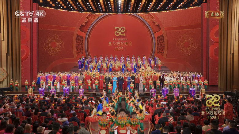 A massive LED stage bathed in saturated red and gold, featuring synchronized dancers in traditional dress