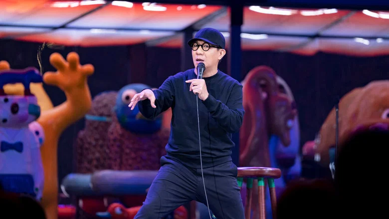 Udom Taephanich on stage, mid-gesture, under warm lighting, a crowd blurred in the background