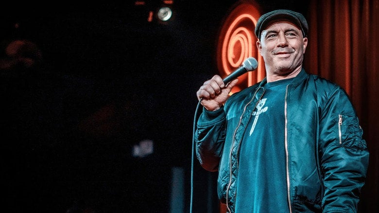 Rogan mid-rant, arms outstretched, sweat glistening under the stage lights