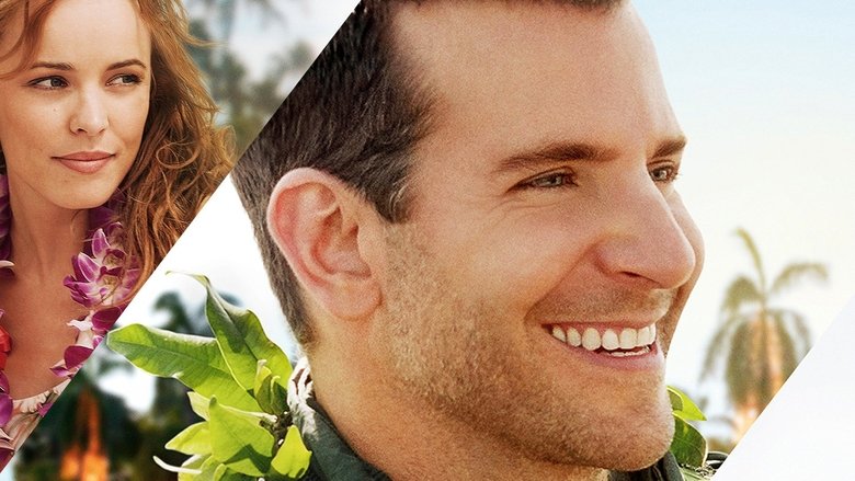 Bradley Cooper and Emma Stone standing on a Hawaiian beach at sunset, the sky a gradient of pink and orange