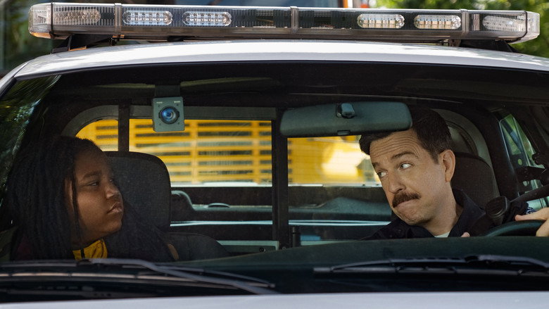 A tense standoff in a dimly lit Detroit alley, with Ed Helms and Terrence Little Gardenhigh back-to-back, surrounded by shadowy figures.