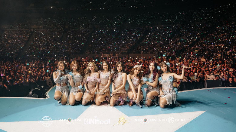 The members of BINI stand in a line on an empty stage, bathed in stark light, their faces a mix of determination and fatigue.
