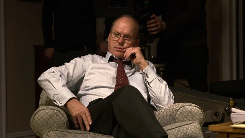 Michael Keaton as Kenneth Feinberg, seated at a long table in a sterile government office, his face half-lit by the cold glow of a laptop screen