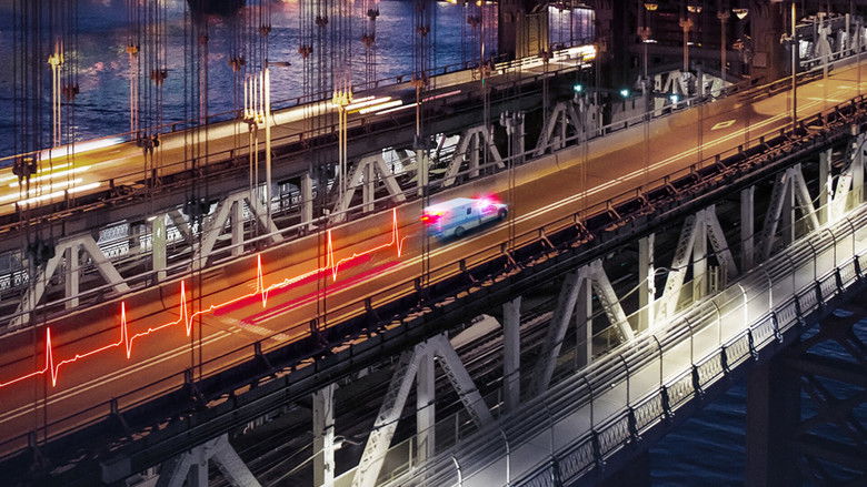 A helicopter paramedic team rushing toward a waiting ambulance under the glow of city lights